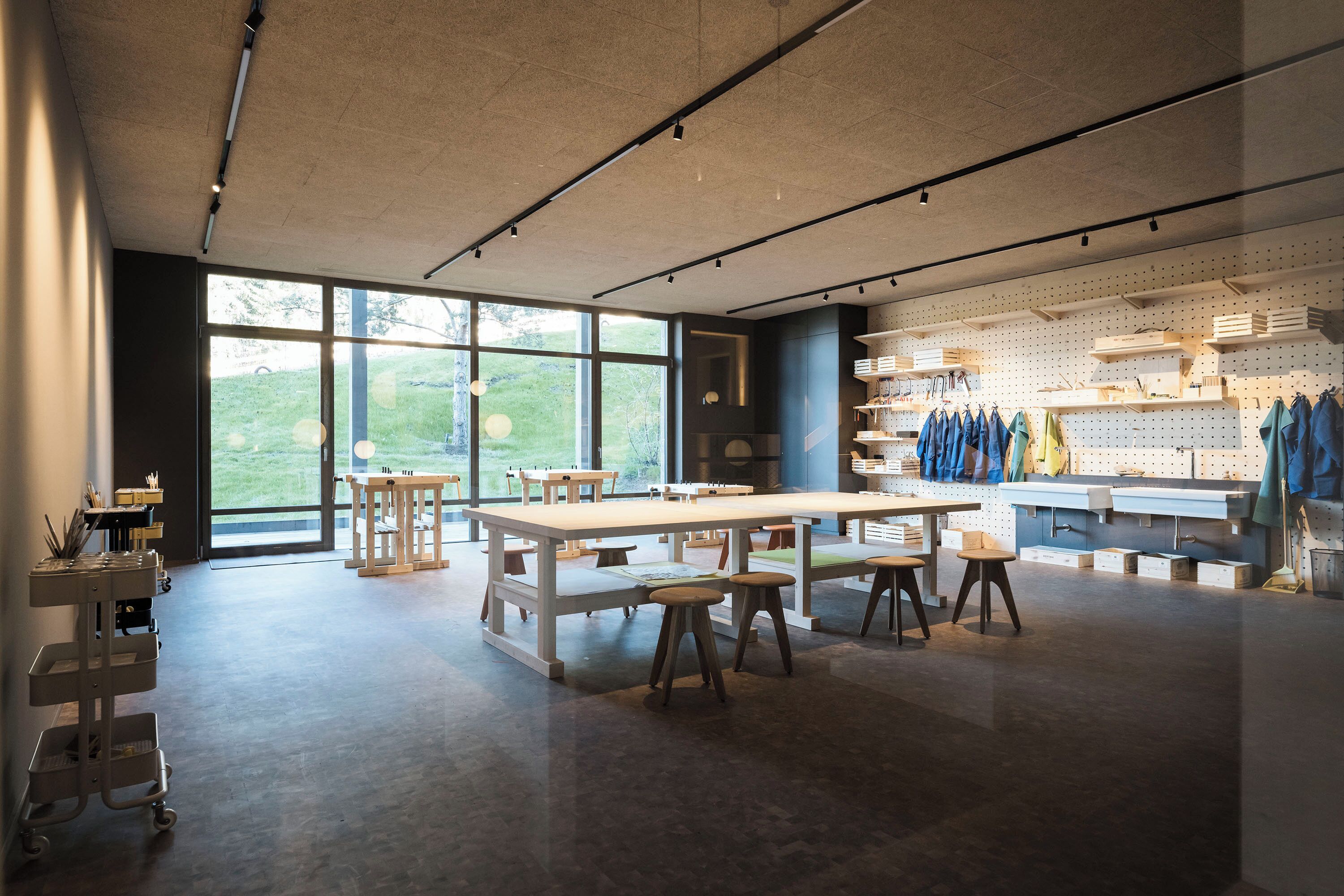 A spacious room with large windows, a central table, and a pegboard wall with hanging items.