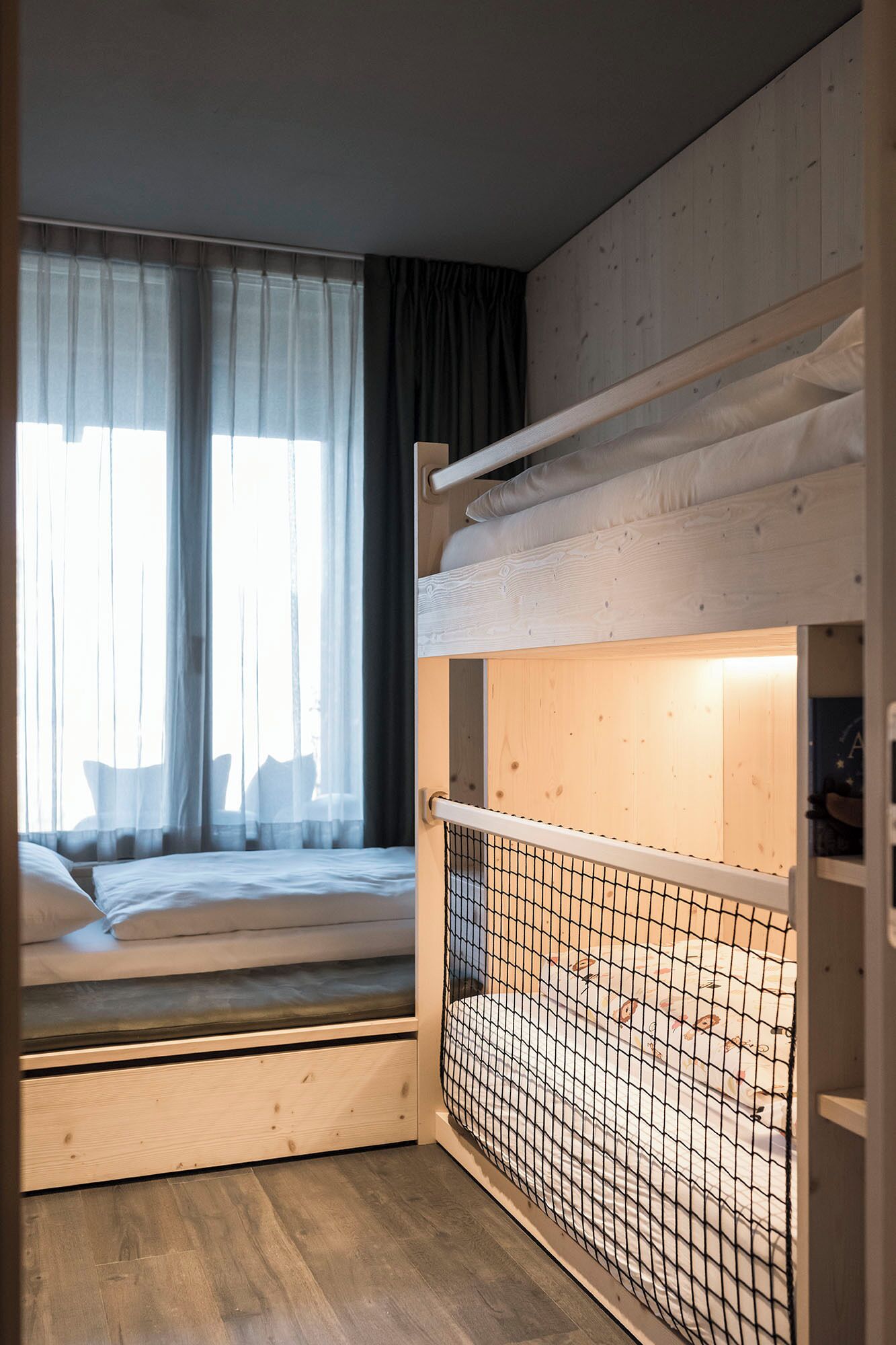 A bunk bed with a wooden headboard and a window with sheer curtains.