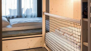 A bunk bed with a wooden headboard and a window with sheer curtains.