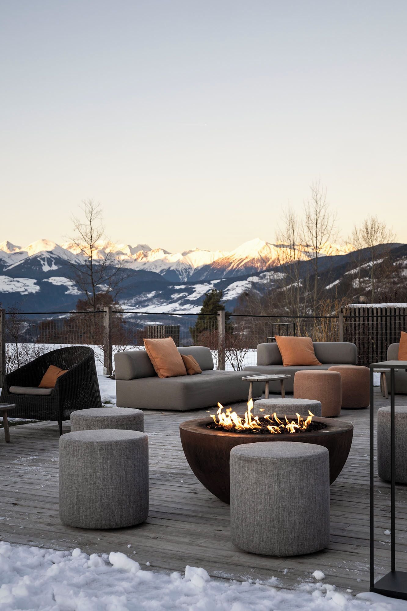 Une terrasse avec coin salon extérieur, un foyer et une vue sur des montagnes enneigées.