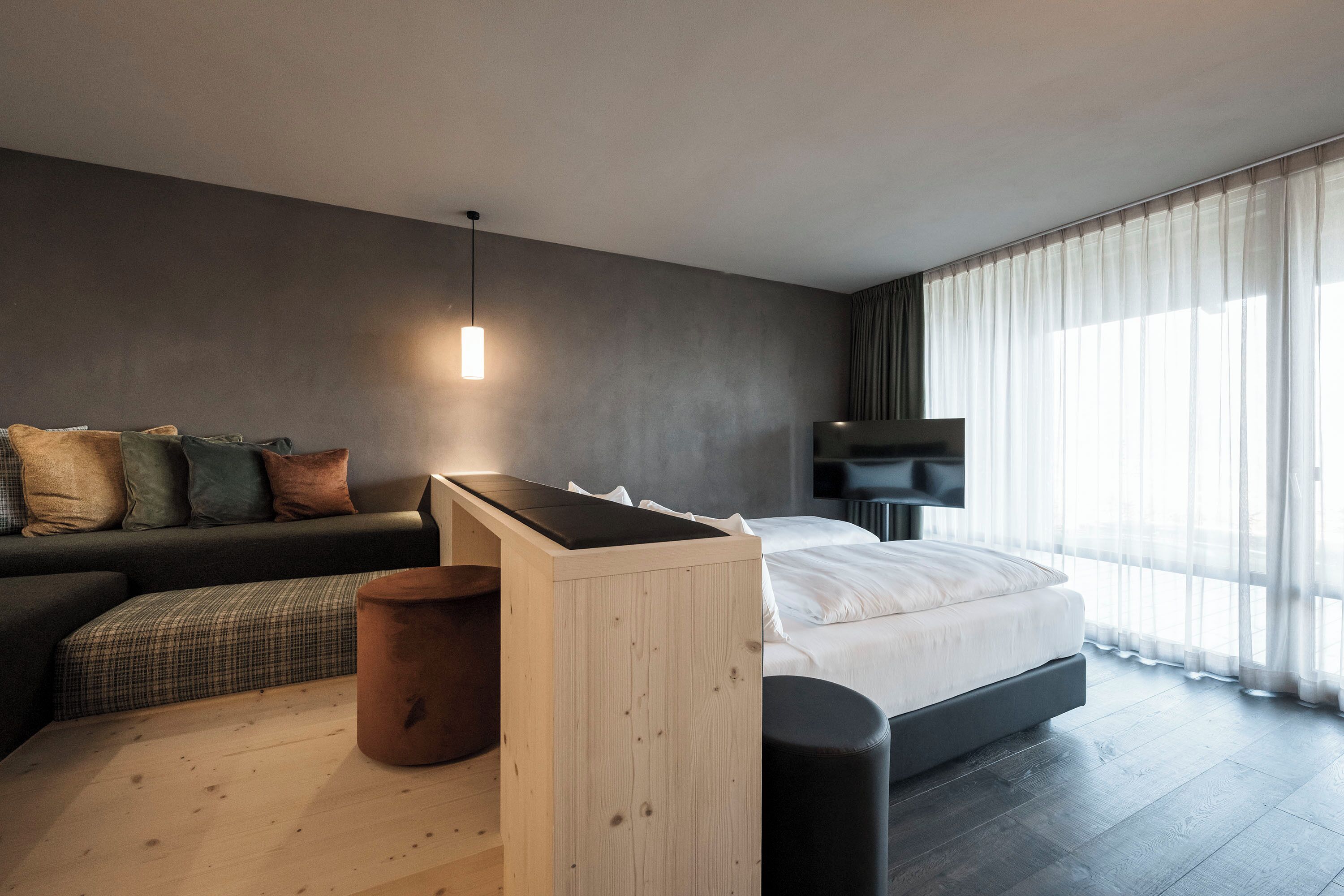 Een moderne hotelkamer met een bed, een bank, een houten bijzettafeltje en een televisie.