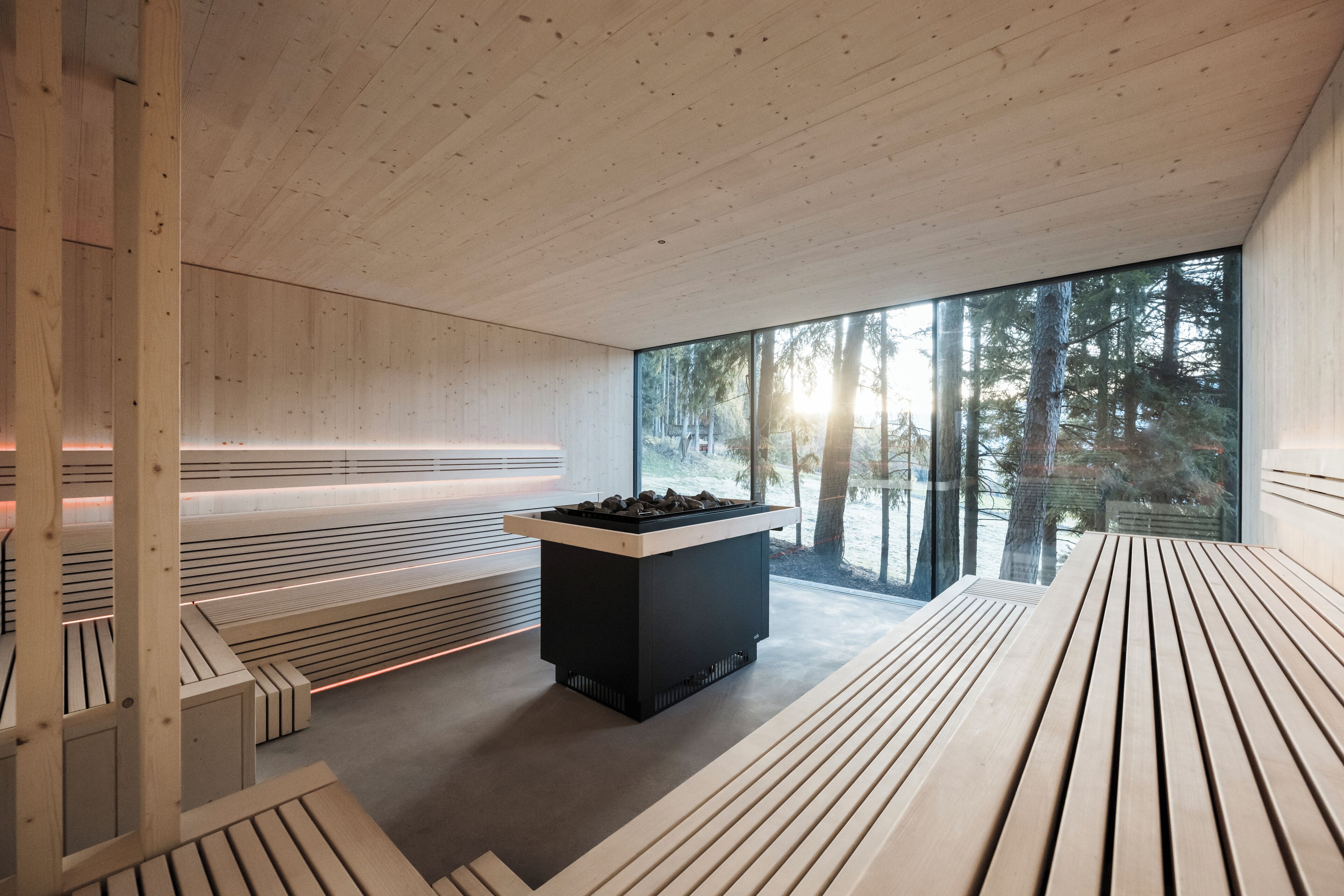 Un intérieur moderne avec des bancs en bois à lattes, une table noire au centre et de grandes fenêtres donnant sur une forêt.