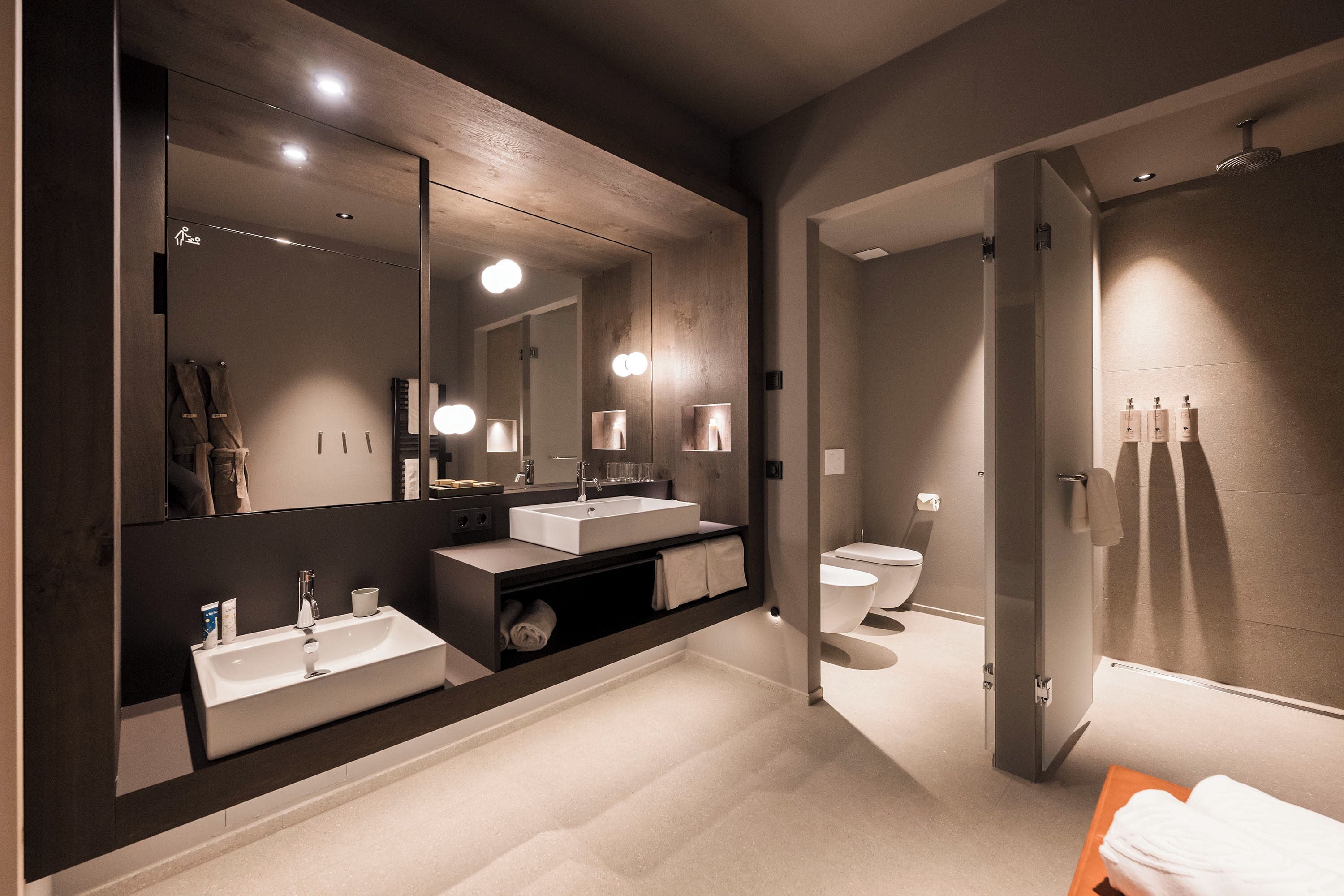 A modern bathroom with a large mirror, two sinks, a toilet, and a shower area.