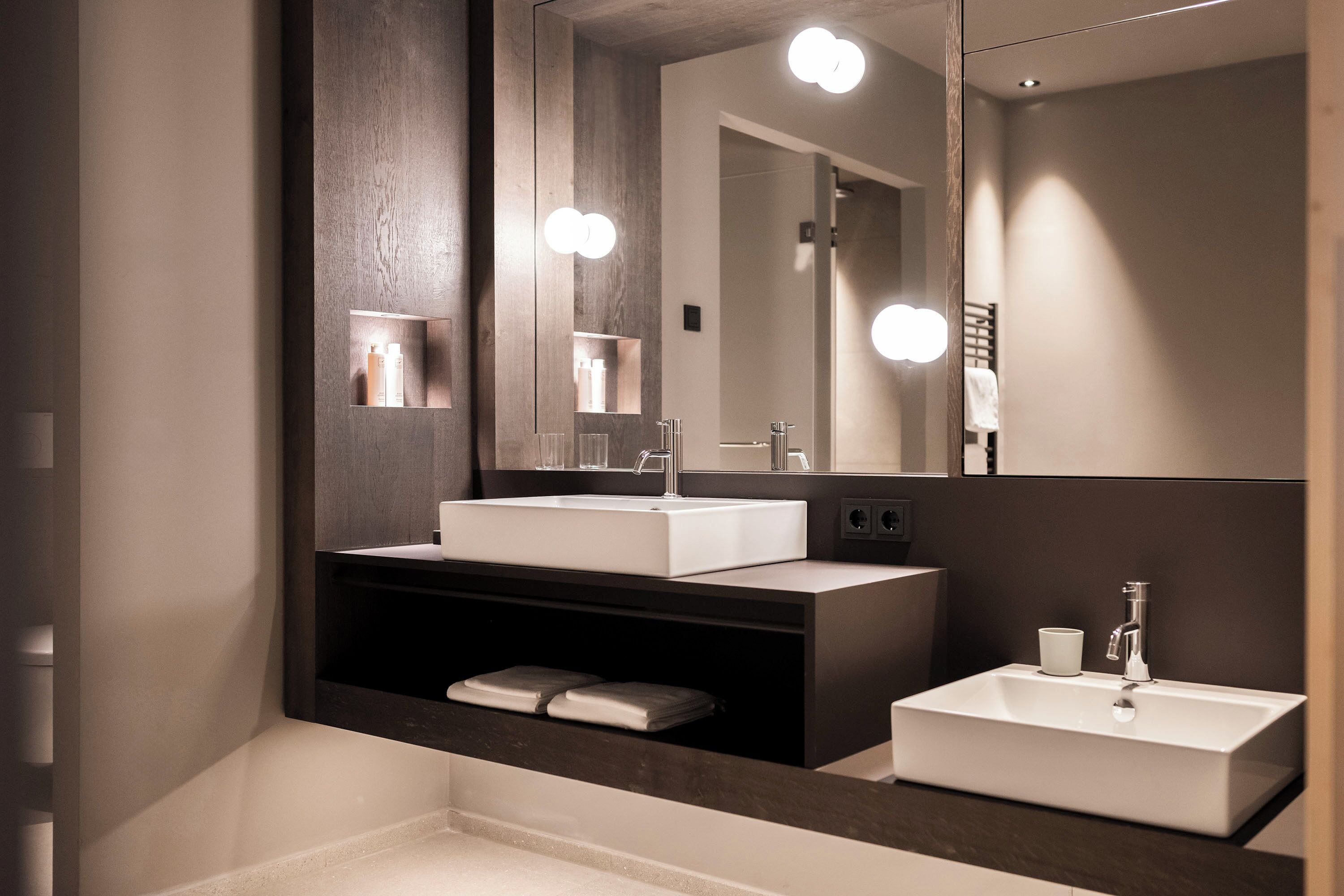 A modern bathroom with two sinks, a large mirror, and built-in shelves.