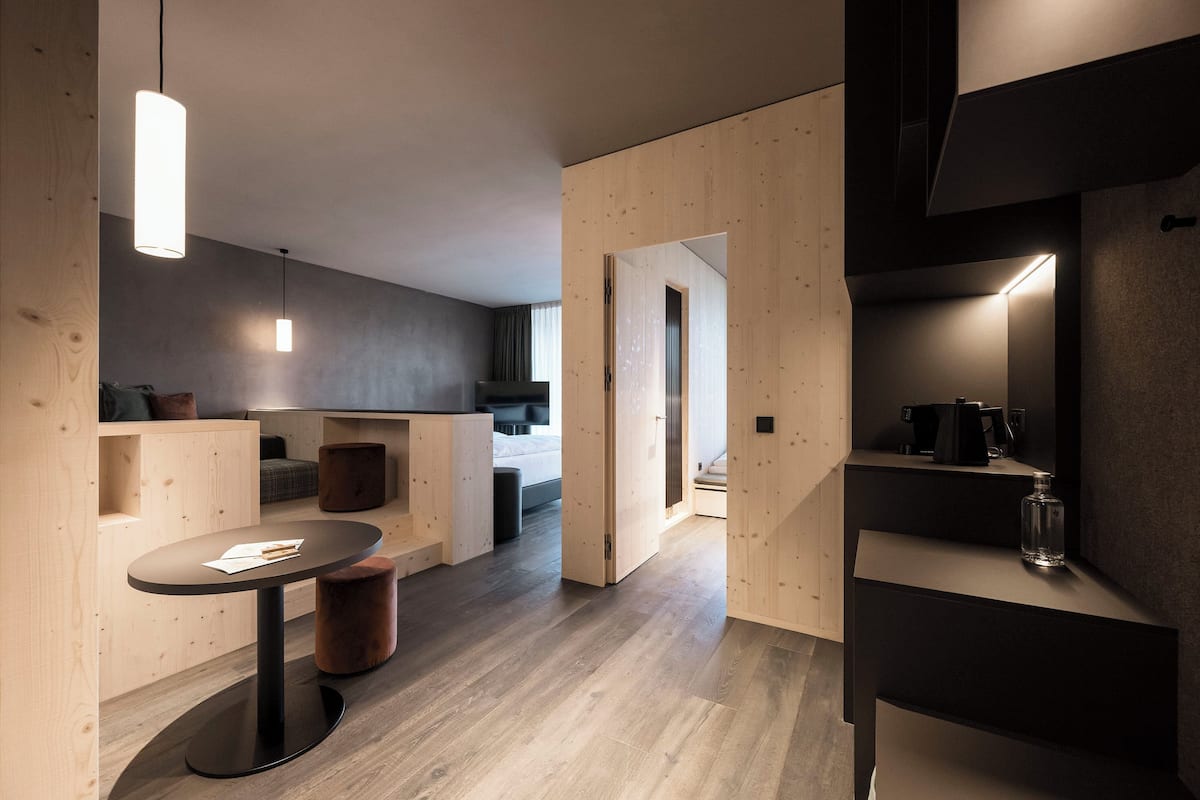 A modern, minimalist room with a wooden floor, a round table with a black base, and a hanging light fixture.