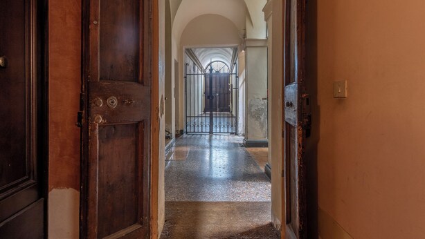 A corridor with a wooden door on the left, a metal gate at the end, and a tiled floor. - HouSmart Moline 20 (Bologna)