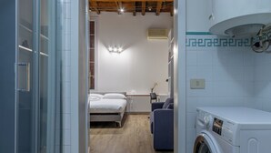 A compact hotel room with a bed, a washing machine, and a small seating area. - HouSmart Moline 20 (Bologna)