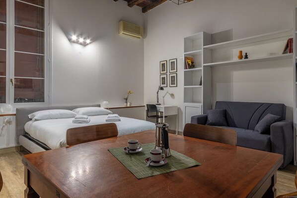 A hotel room with a bed, a desk, a chair, a coffee table, and a bookshelf.