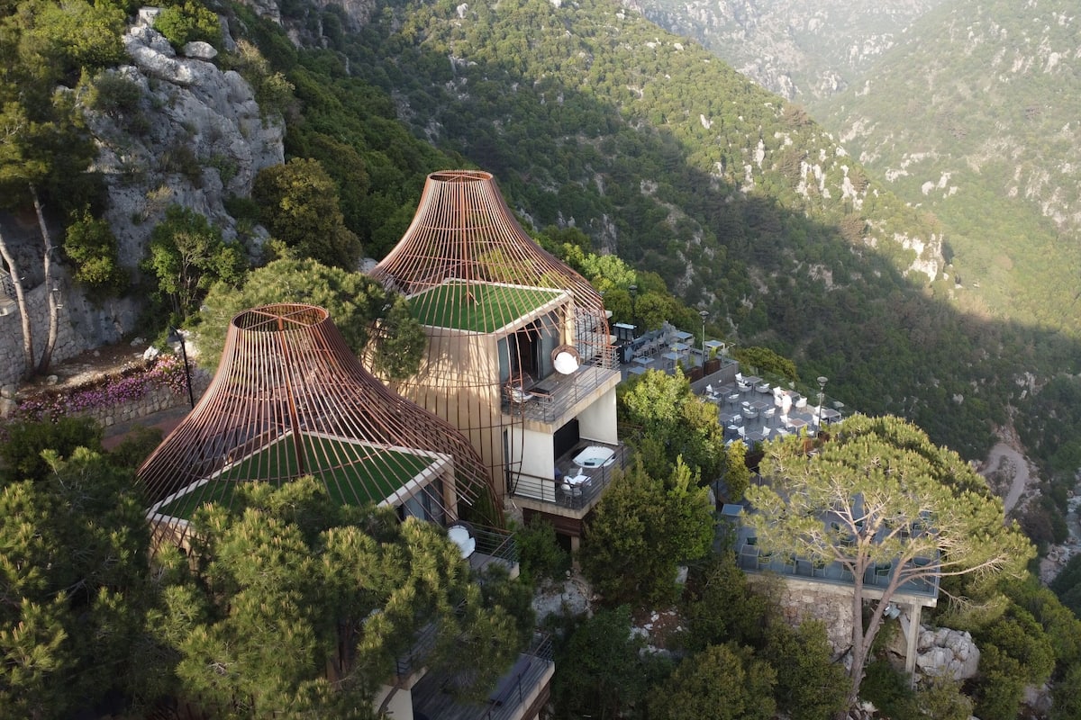 Un hotel moderno con una estructura de techo cónica distintiva, ubicado en una colina con exuberante vegetación y un río al fondo.
