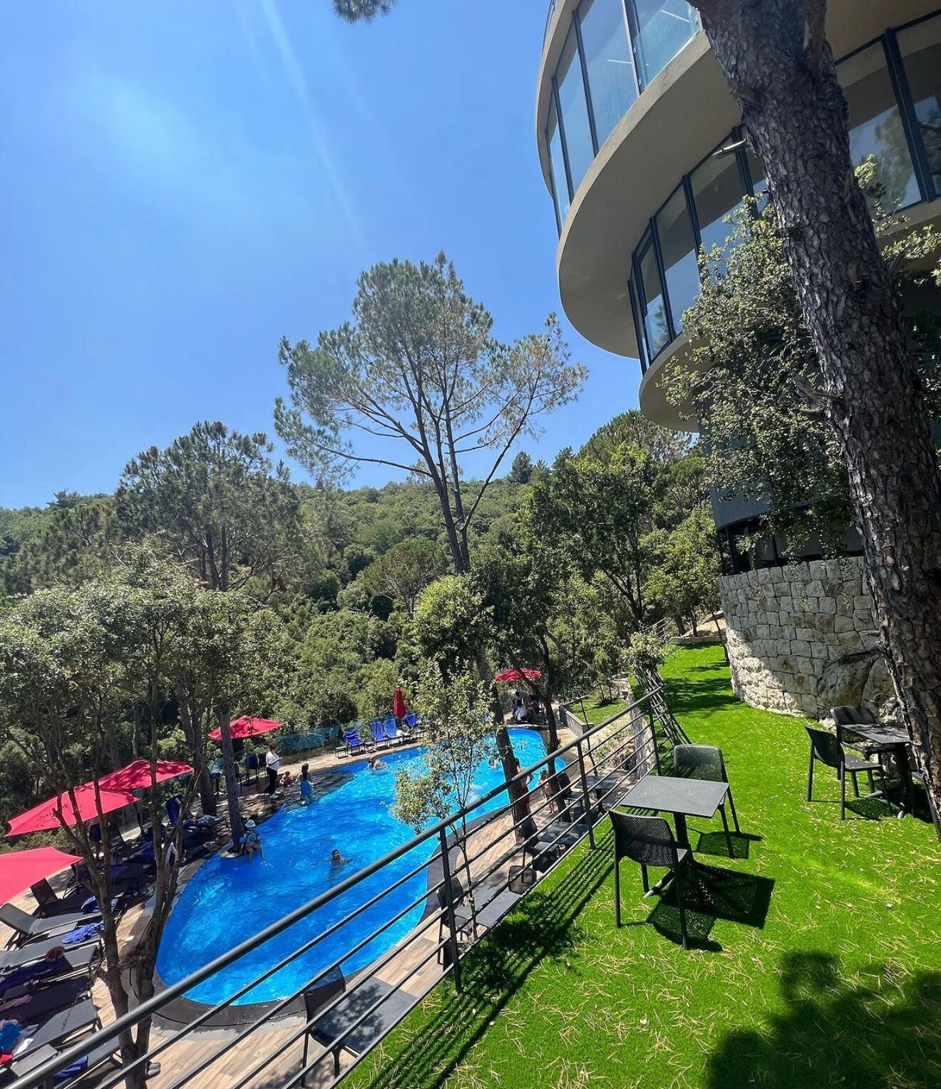 A pool area with a clear blue pool, surrounded by green grass and trees, and a stone wall.