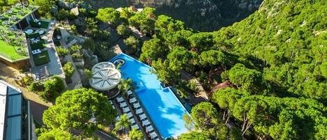 An aerial view of a resort with a swimming pool surrounded by lush greenery and a mountainous backdrop.