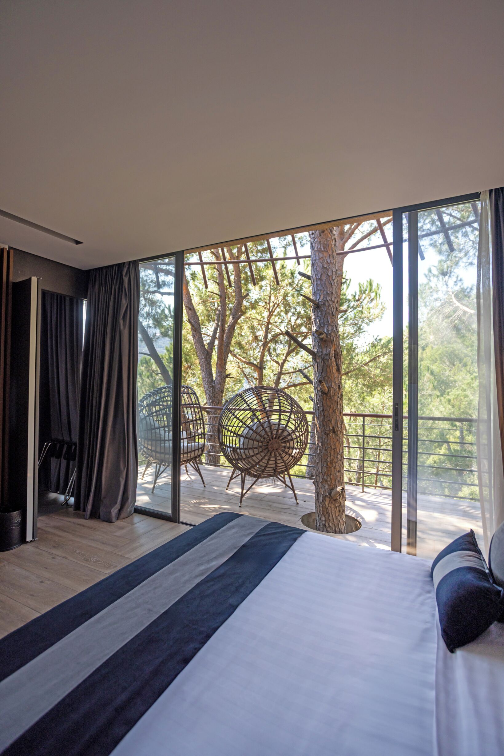 Une chambre moderne avec un grand lit, une vue sur les arbres et un balcon équipé de chaises.