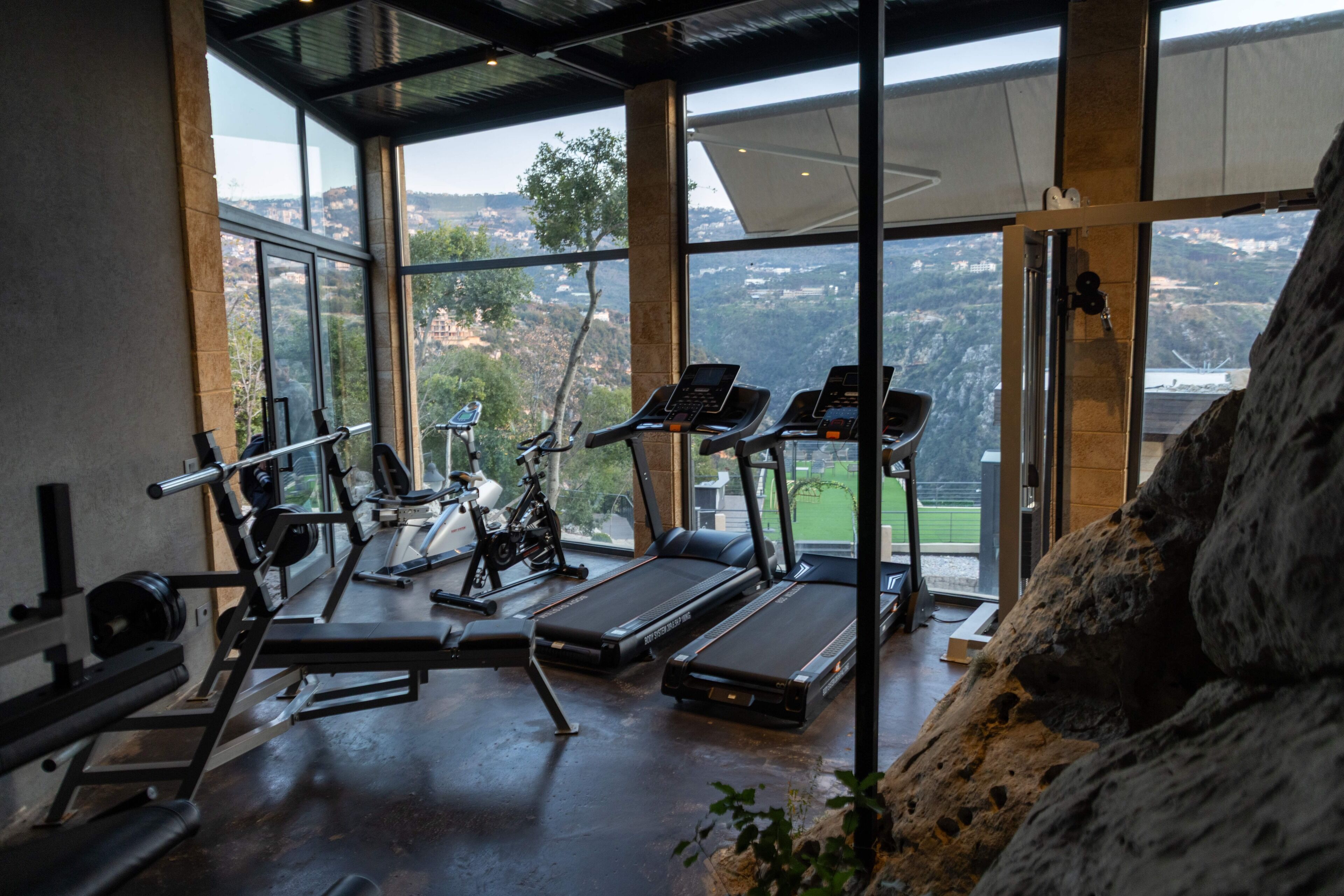 A gym with exercise equipment and large windows offering a view of the outdoors.