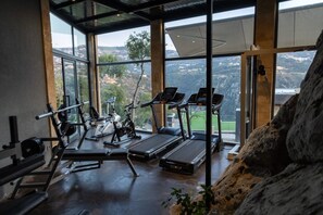 A gym with exercise equipment and large windows offering a view of the outdoors. - Scappa Resort (Ajaltoun)