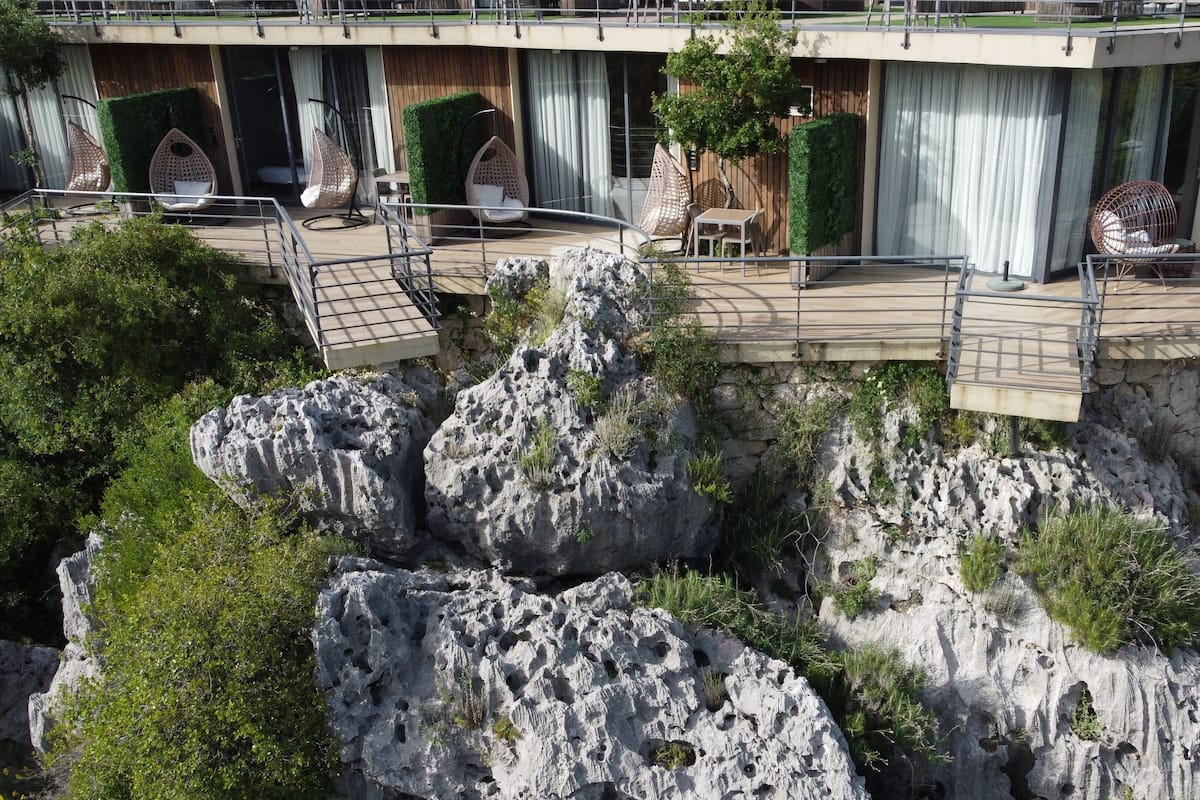 Un hotel con balcón que da a un acantilado rocoso, amueblado con sillones de mimbre y una mesa.