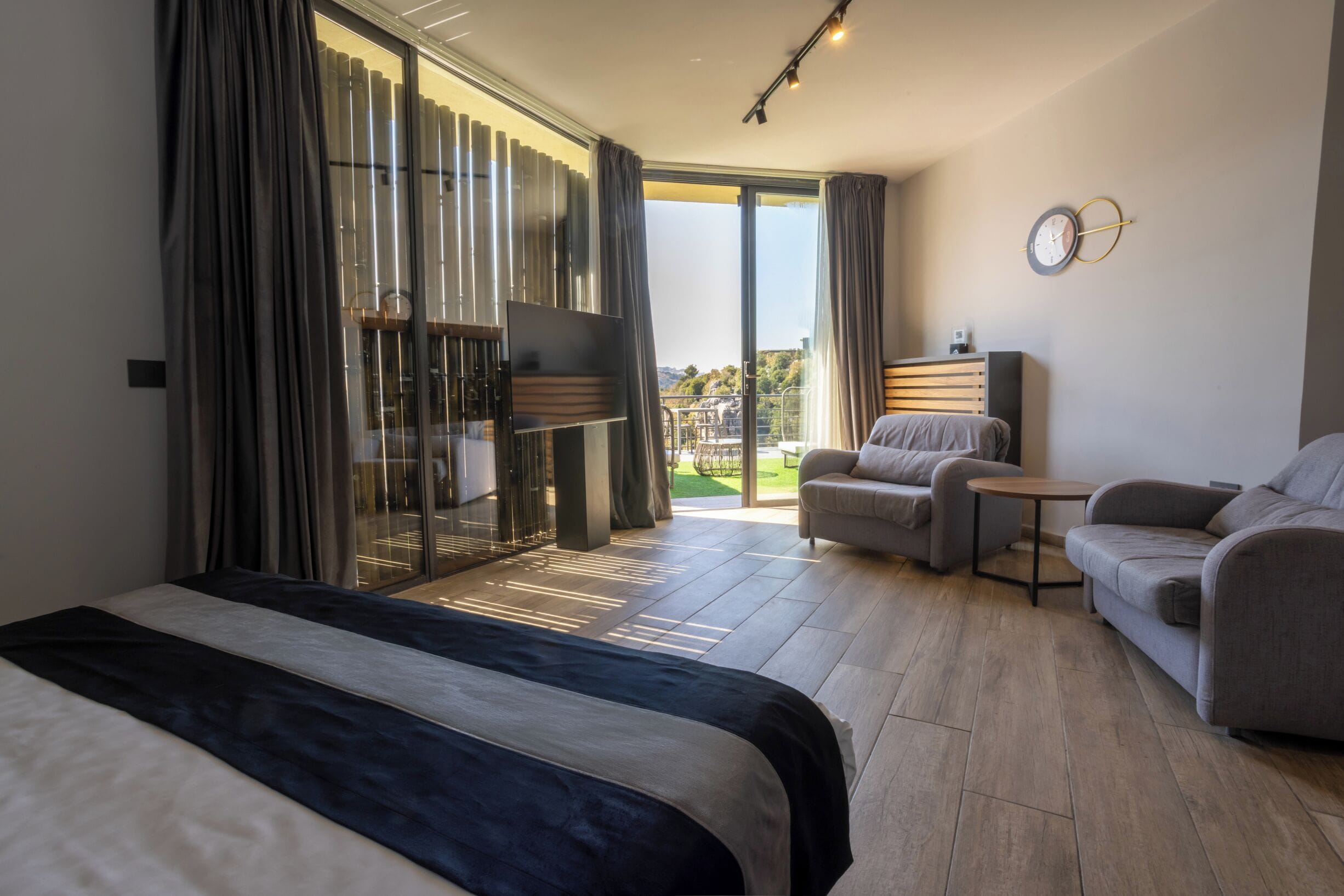 A modern hotel room with a large bed, a sofa, a small table, and a balcony with a view.