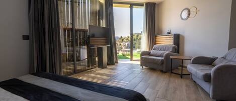 A modern hotel room with a large bed, a sofa, a small table, and a balcony with a view.