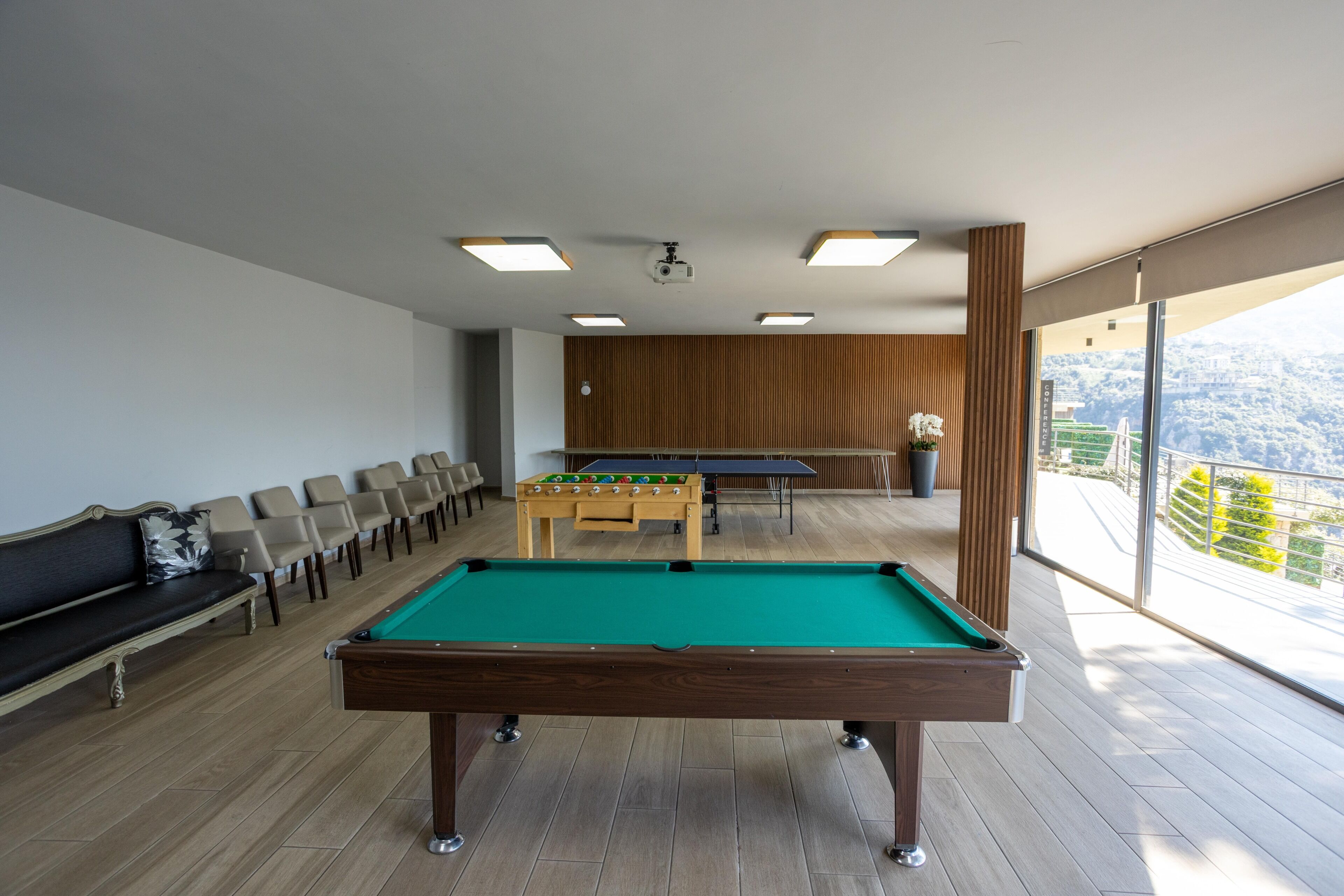 A pool table in a room with a view, a foosball table, and a sofa.