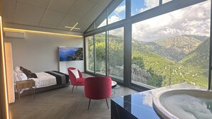 A modern hotel room with a large window, a bed, a red chair, and a hot tub. - Scappa Resort (Ajaltoun)