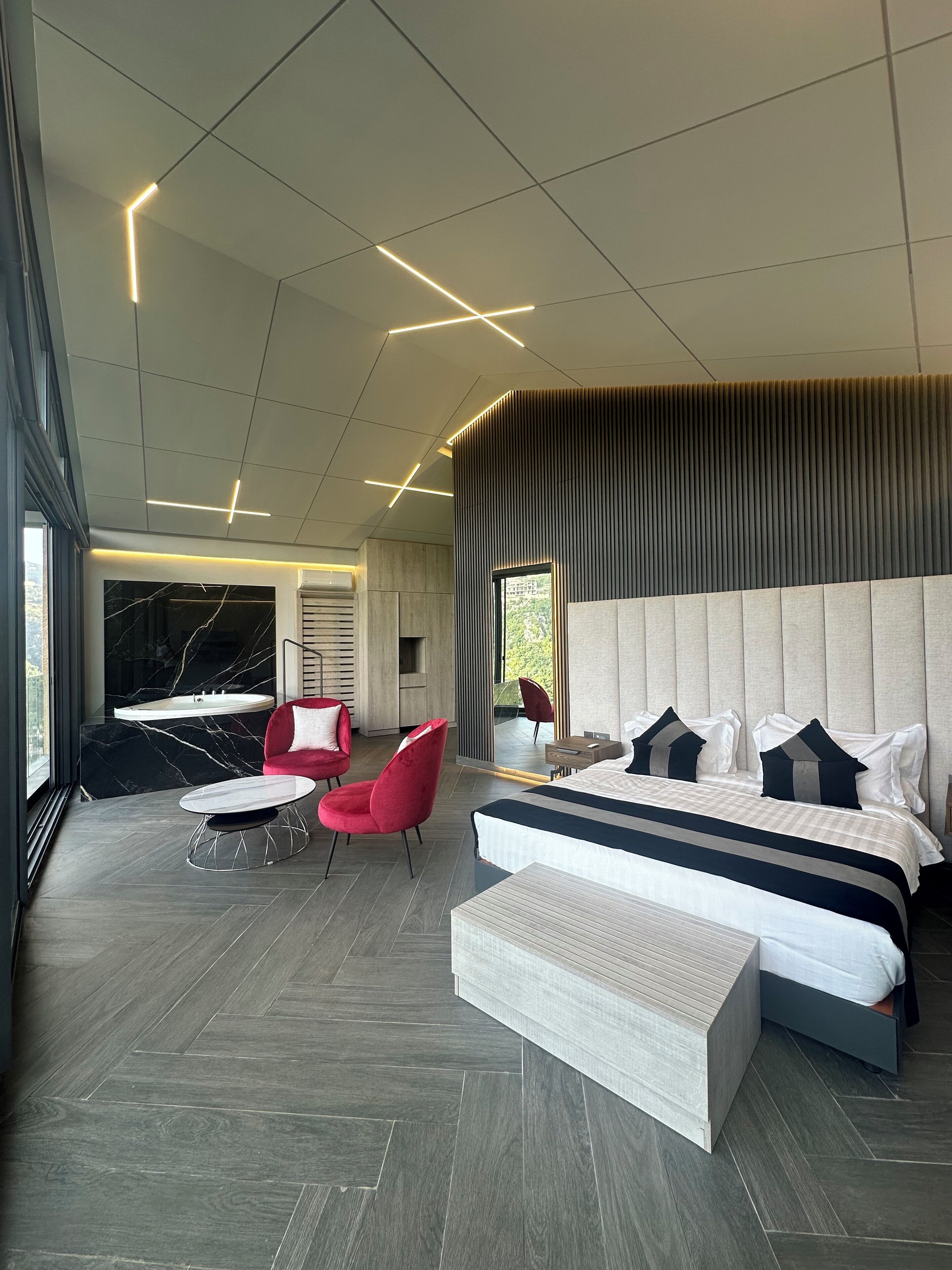Un dormitorio moderno con una cama grande, una silla roja, una mesita y vistas al exterior.