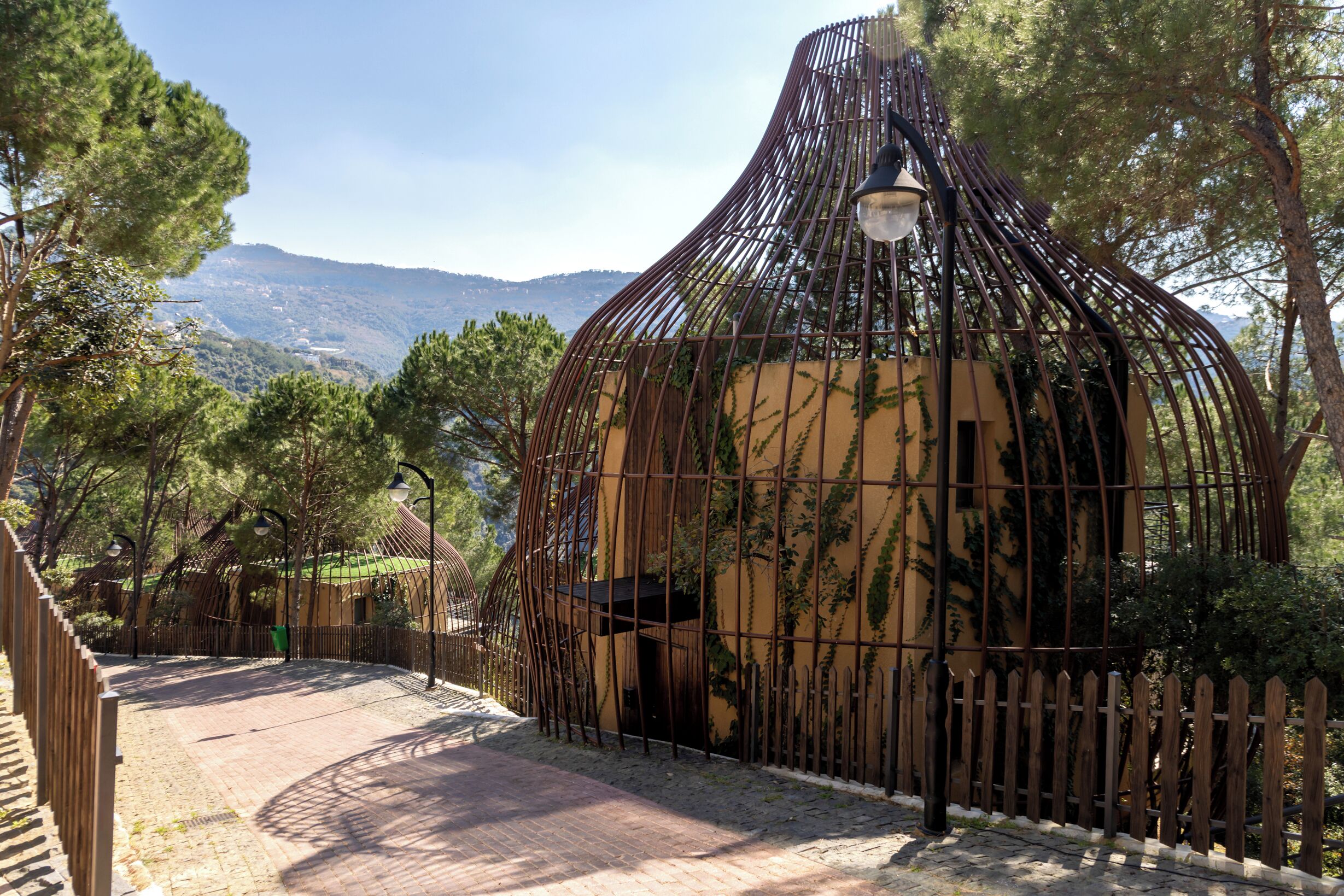 Un edificio rústico con una estructura metálica distintiva, rodeado de árboles y un camino adoquinado.
