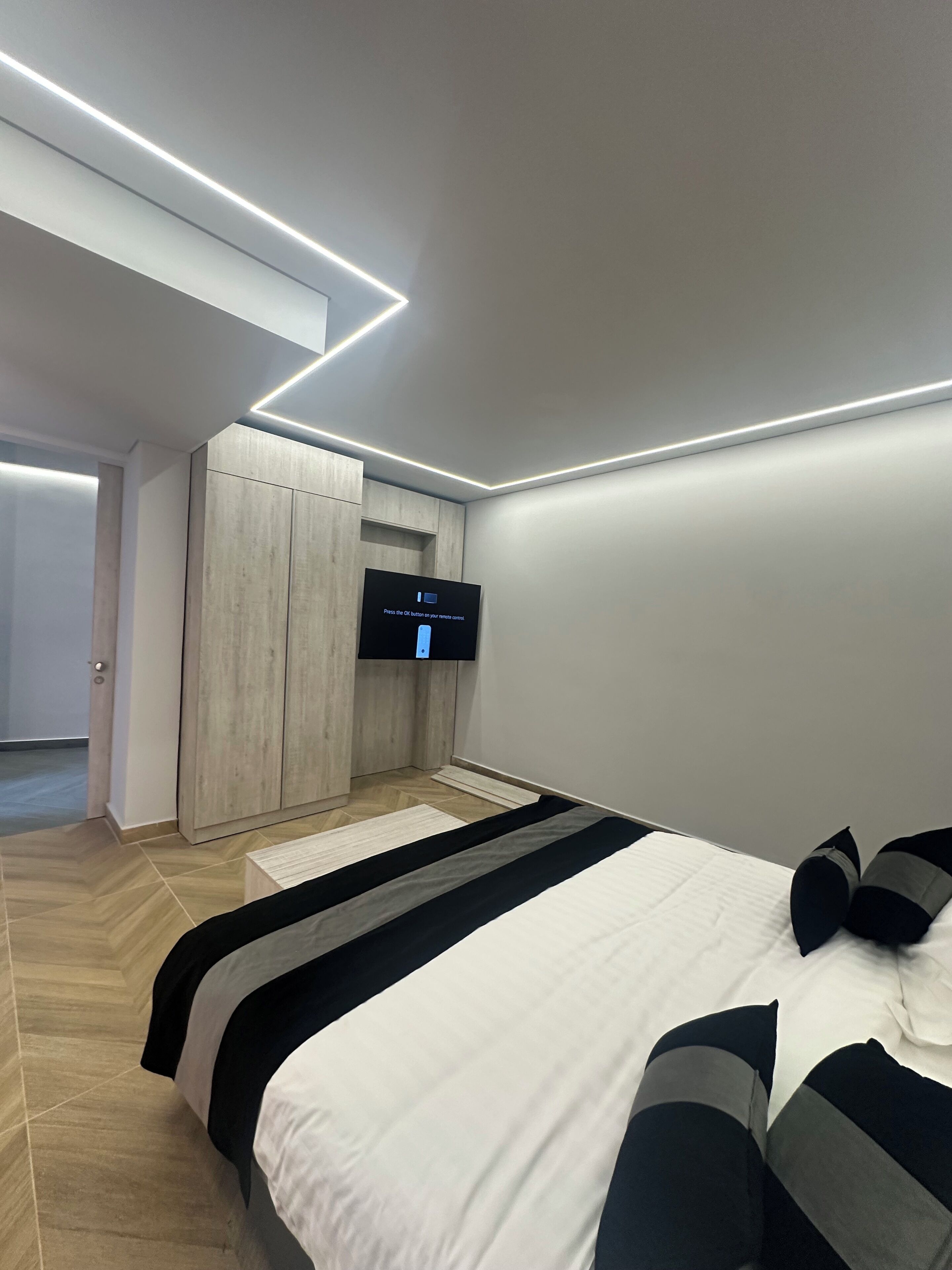Quarto moderno com cama, TV na parede e guarda-roupa.