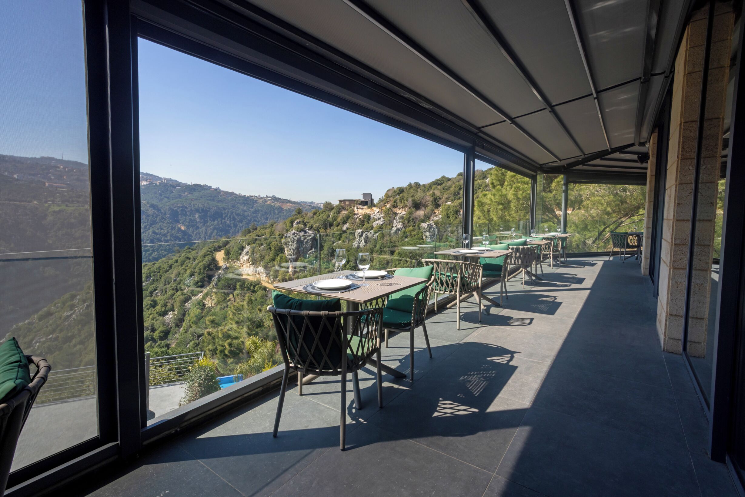 An outdoor terrace with tables and chairs, offering a view of a hilly landscape.