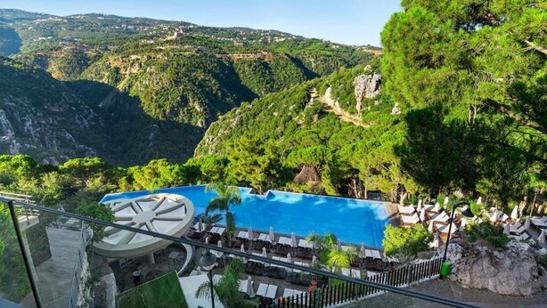 A pool area with lounge chairs and umbrellas, surrounded by lush greenery and hills. - Scappa Resort (Ajaltoun)