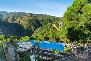 Un área de piscina con sillas de descanso y sombrillas, rodeada de exuberante vegetación y colinas.
