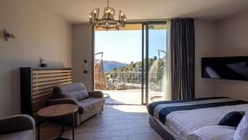 Une chambre d’hôtel moderne avec un grand lit, un canapé, une petite table et un téléviseur. La chambre dispose d’un balcon avec vue sur les montagnes.