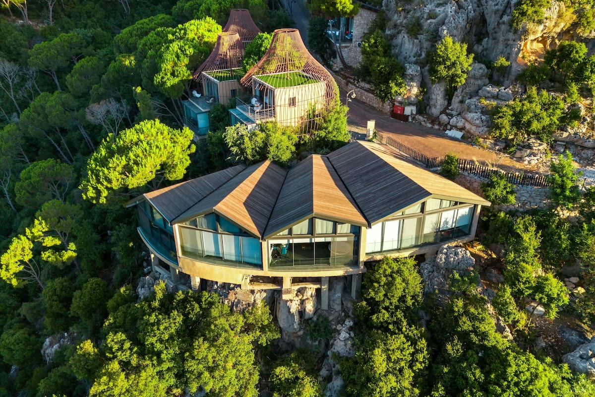 Una casa moderna con un techo curvo singular, rodeada de exuberante vegetación y terreno rocoso.