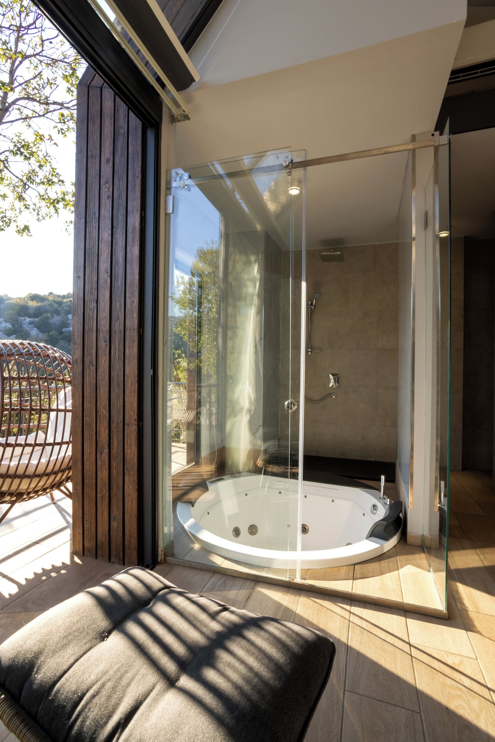 A glass-enclosed shower area with a built-in bathtub, wooden flooring, and a view of the outdoors.