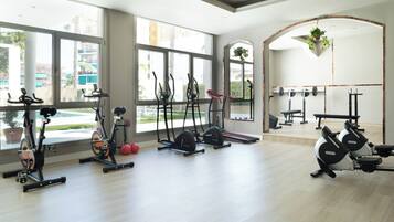 Un gimnasio con diferentes equipos de ejercicio, ventanas amplias y vista a una piscina.