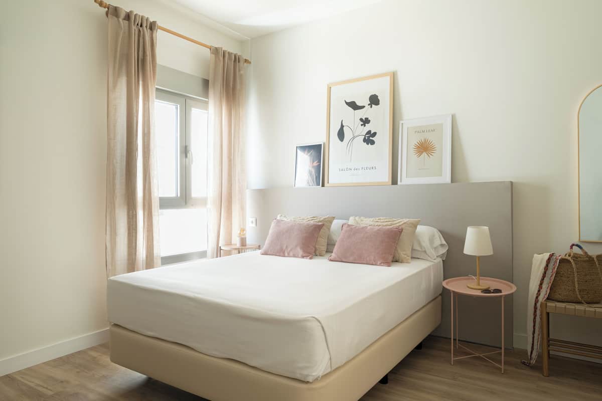 Une chambre à coucher bien rangée, avec un grand lit, une table de chevet avec une lampe et un miroir fixé au mur.