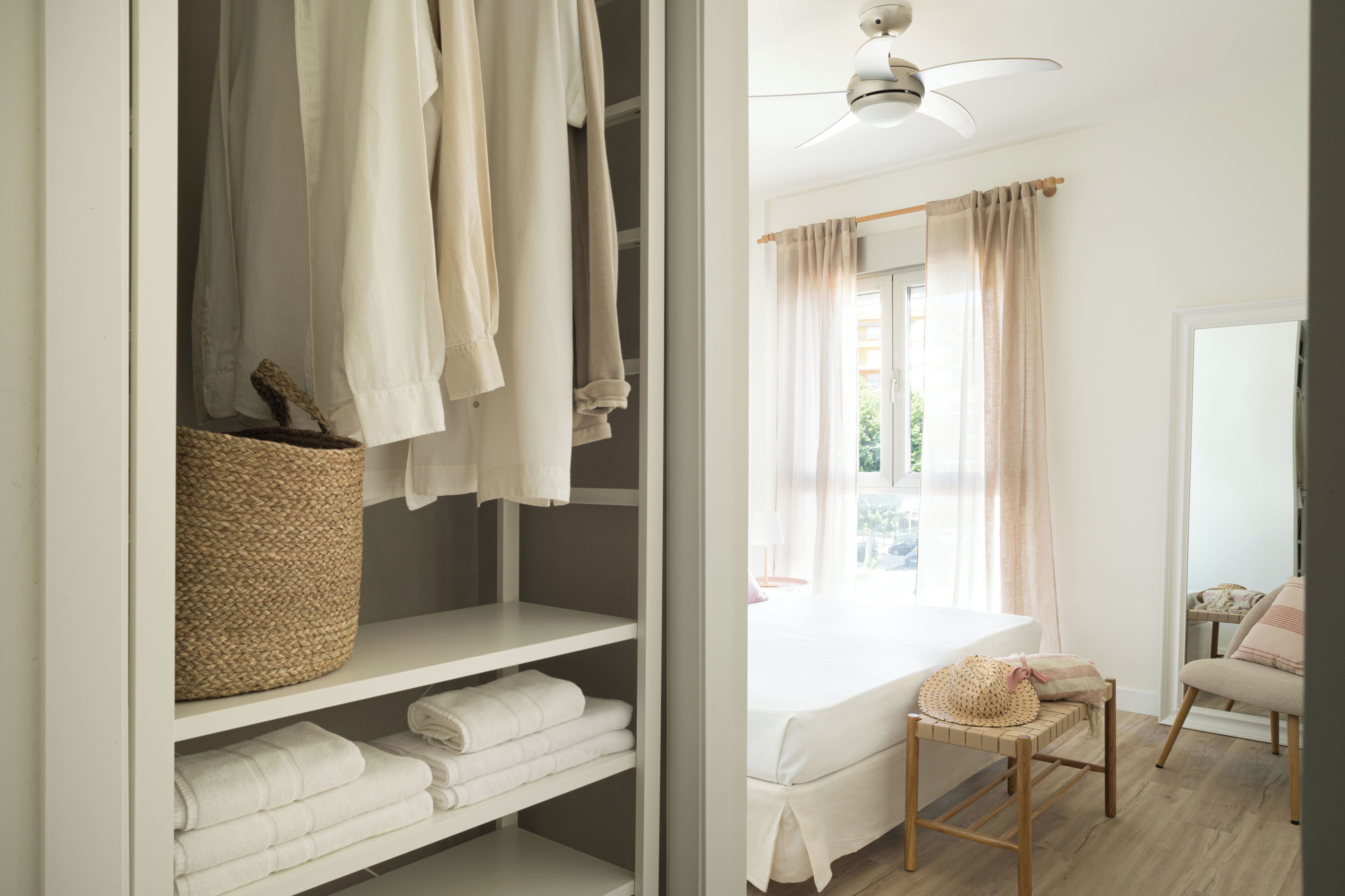 A bedroom with a bed, a chair, a bedside table, a ceiling fan, and a closet with shelves and a basket.