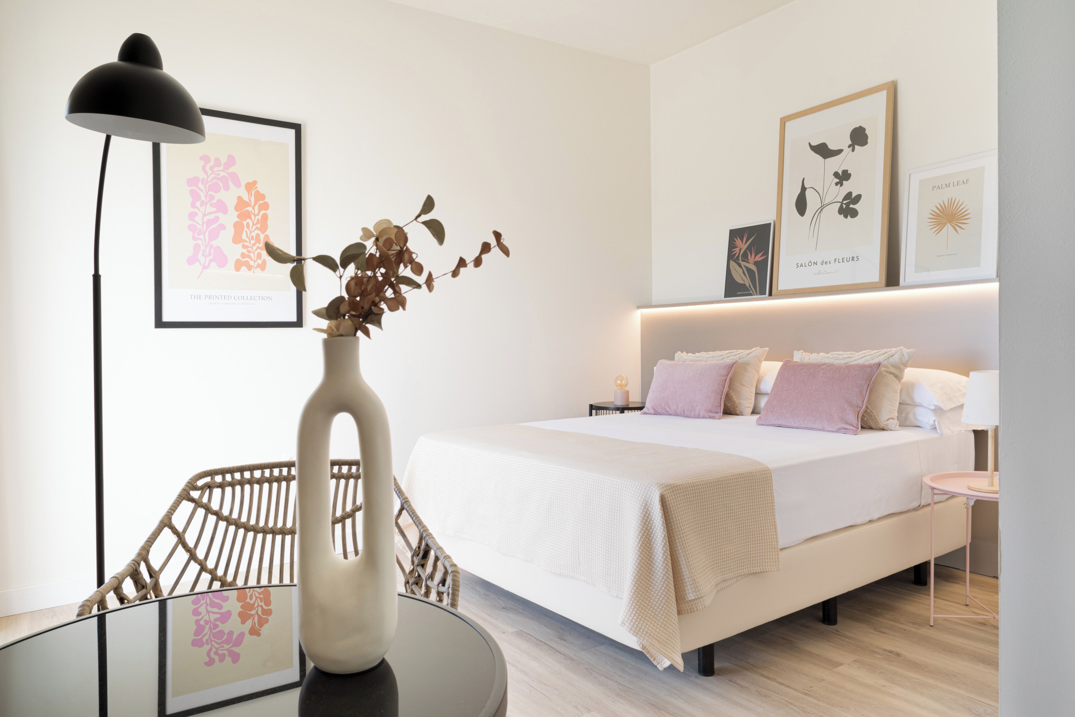 Een moderne slaapkamer met een groot bed, nachtkastjes, een vloerlamp en wanddecoratie.
