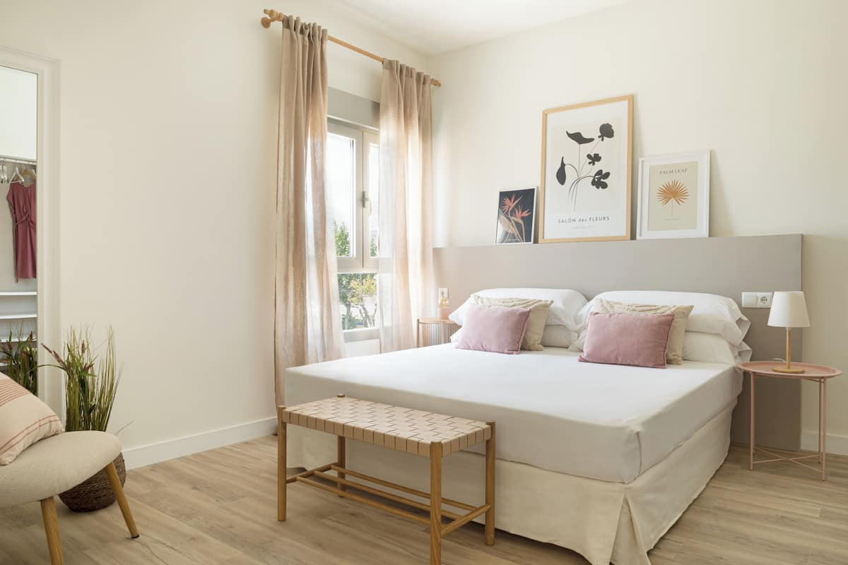 Une chambre à coucher avec un lit, une table de chevet, un banc et une fenêtre avec des rideaux.