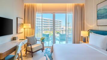 A hotel room with a bed, a desk, a chair, a TV, and a balcony with a view of a building.