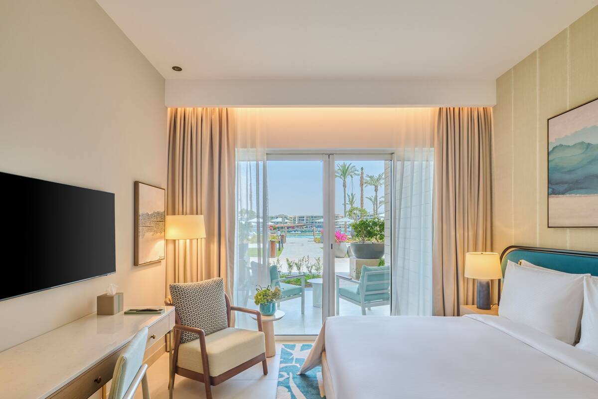 A hotel room with a bed, a desk, a chair, a TV, a window with curtains, and a view of the outside.