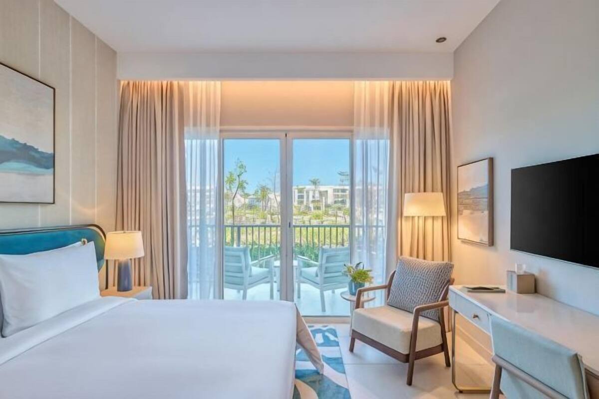 A hotel room with a bed, desk, chair, TV, and a balcony with a view.