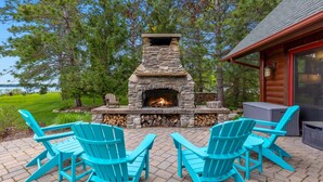 Une cheminée en pierre avec un feu, entourée de fauteuils Adirondack turquoise sur une terrasse dallée.