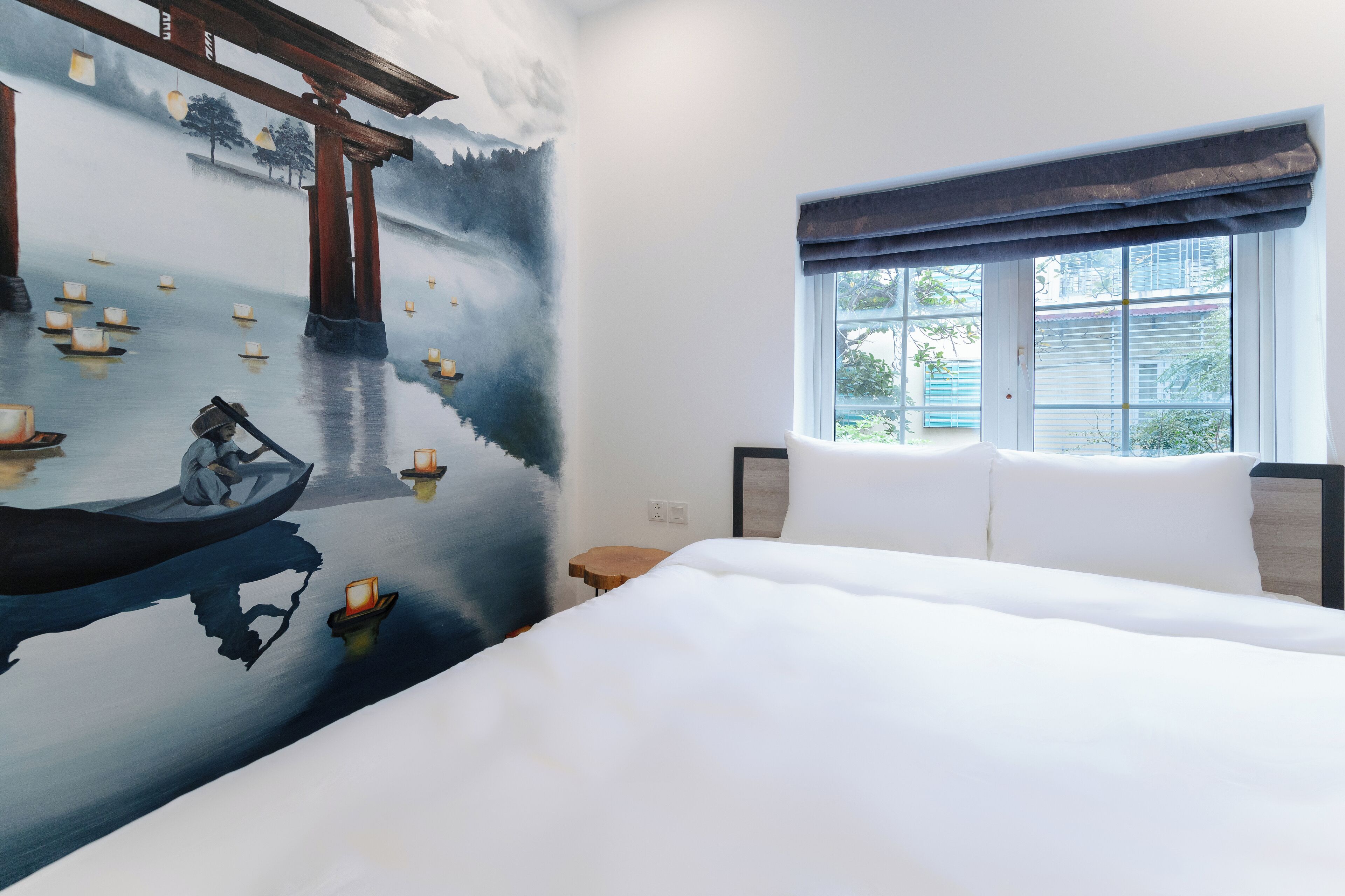 A hotel room with a large bed, a window with a view, and a mural of a serene water scene with boats.