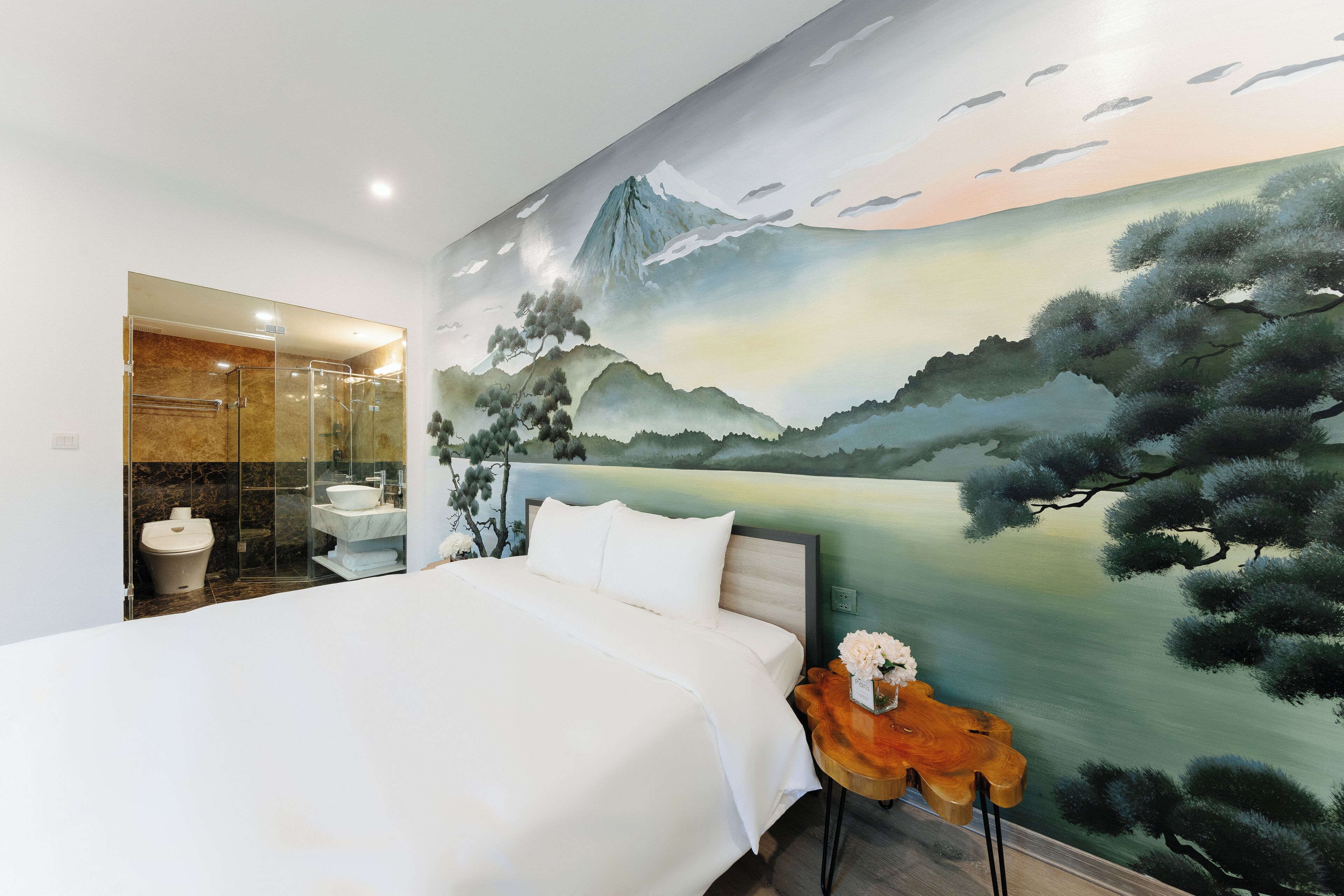 A bedroom with a large bed, a bathroom with a glass shower enclosure, and a mural of a mountain landscape.
