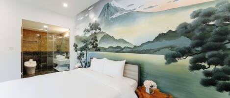 A bedroom with a large bed, a bathroom with a glass shower enclosure, and a mural of a mountain landscape.