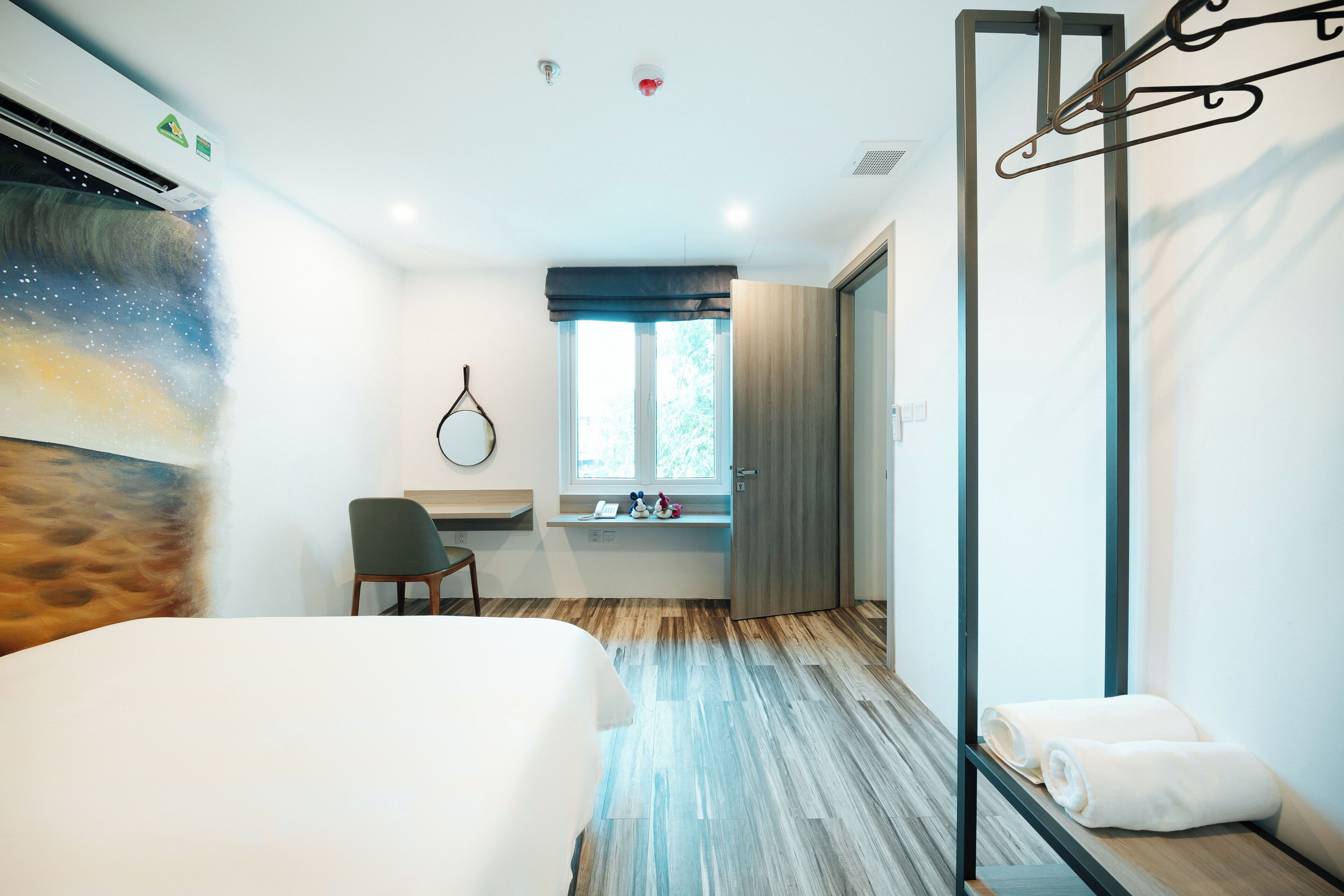 Una camera d'albergo con un letto, una scrivania, una finestra vista e un porta asciugamani a muro.