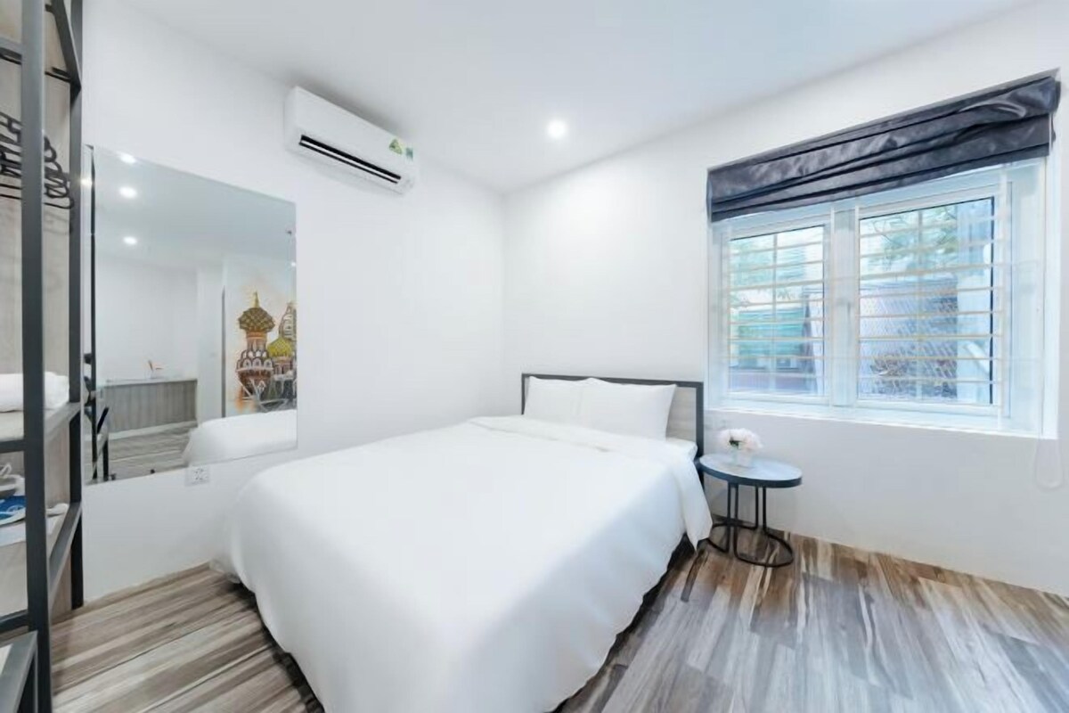 A modern hotel room with a large bed, a small round table, and a window with a view of the outside.