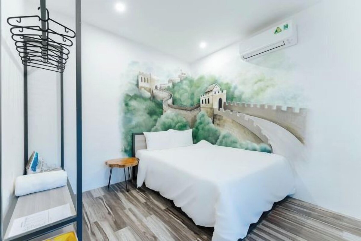 A bedroom with a mural of a castle on the wall, a bed, a bedside table, and a hanging rack.