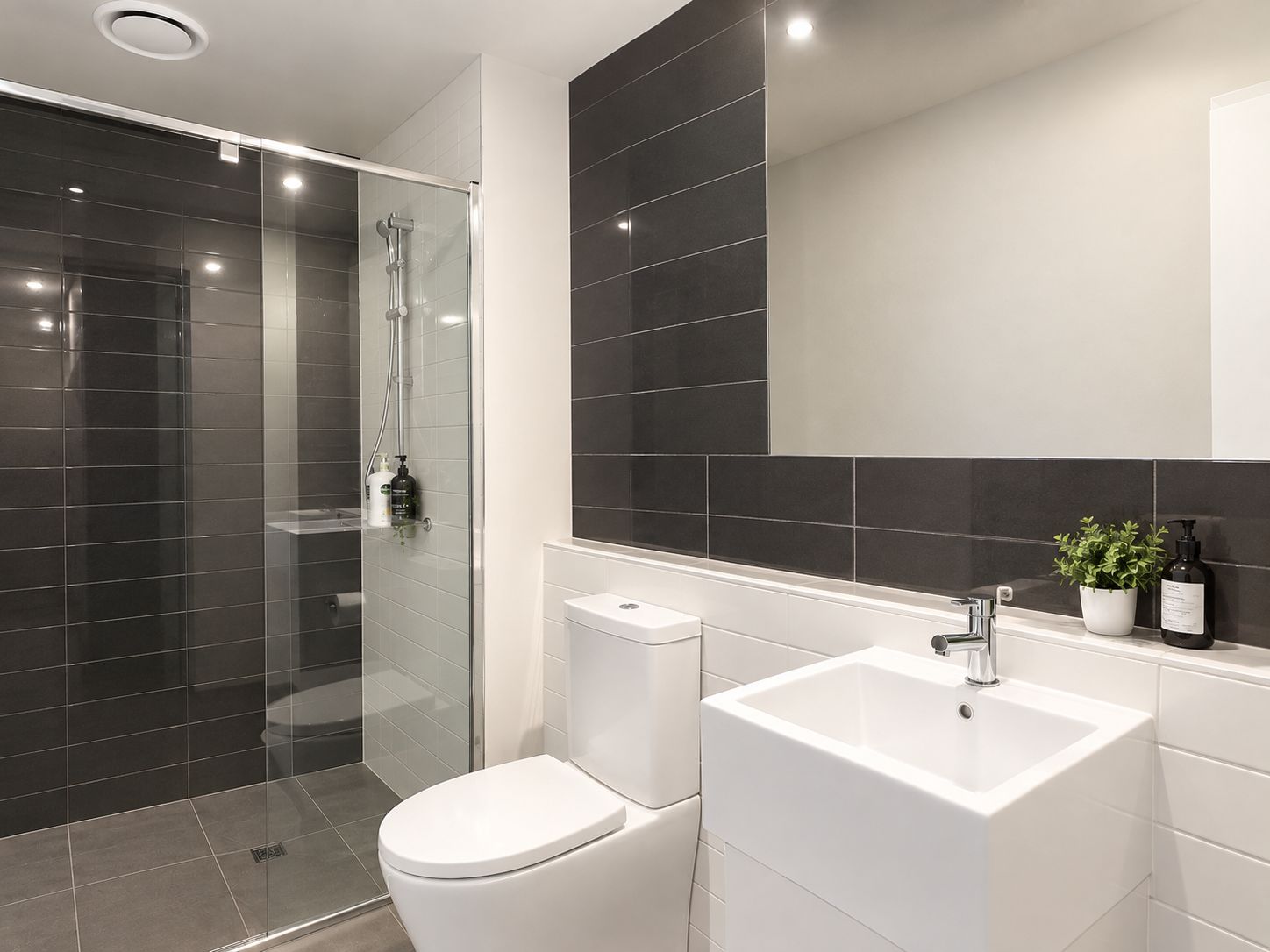 A modern bathroom with a glass shower enclosure, a white toilet, and a white sink with a mirror above it.