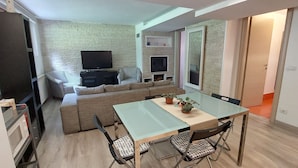 A compact living space with a sofa, a dining table, and a TV. - A LITTLE NEST (Ivrea)