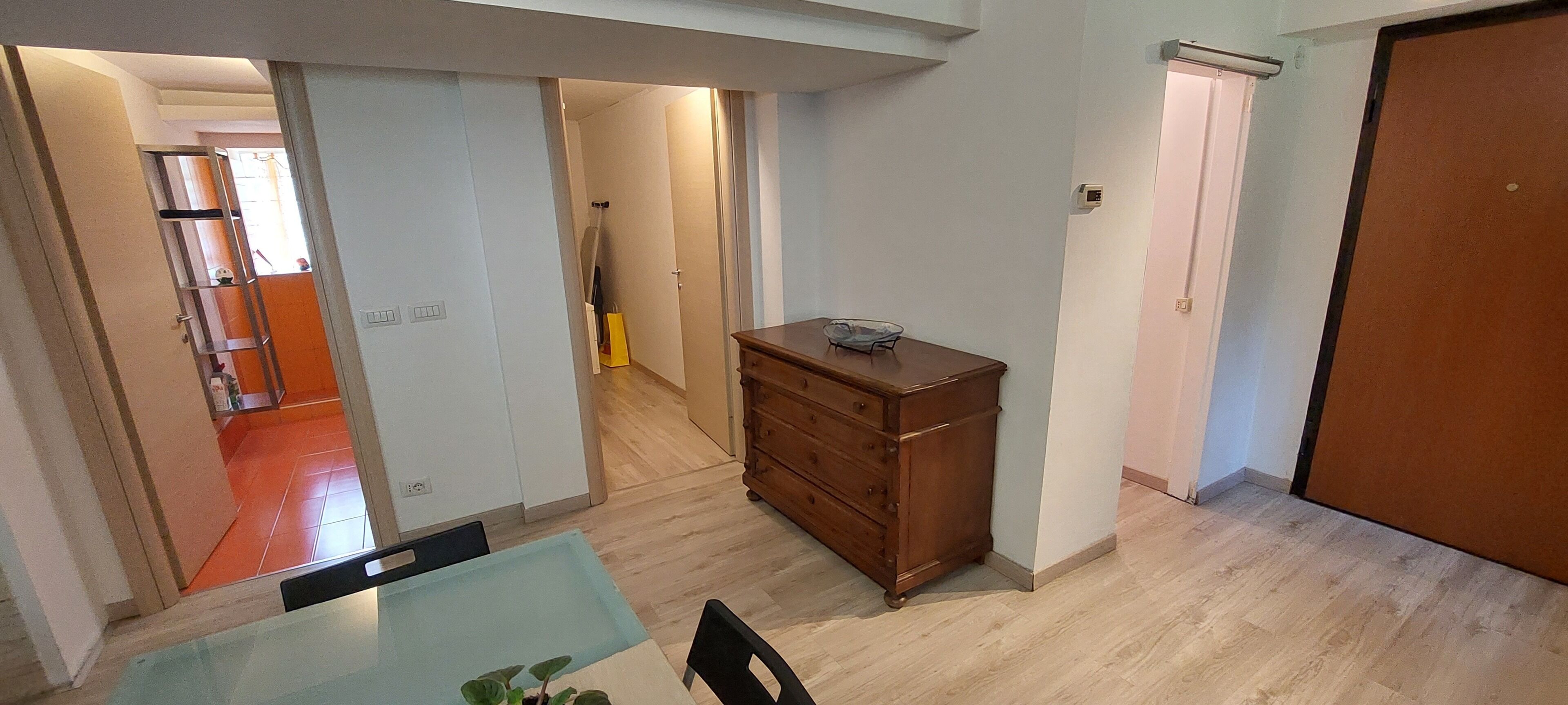 A room with a wooden dresser, a dining table with chairs, and a view of a kitchen area with a red-tiled floor.